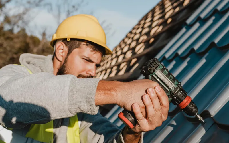 Roofer in a hard hat fastening roofing panels with a cordless drill